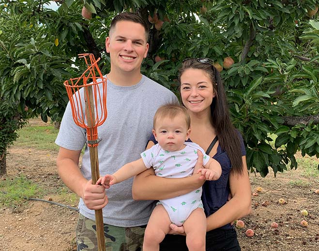 Family holding baby outdoors in orchard